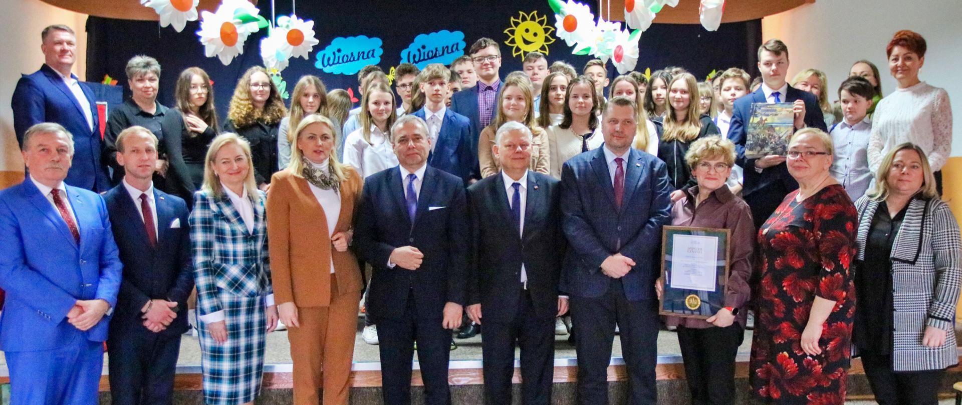 Zbiorowe zdjęcie na pierwszym planie mężczyźni i kobiety, na drugim planie młodzież.