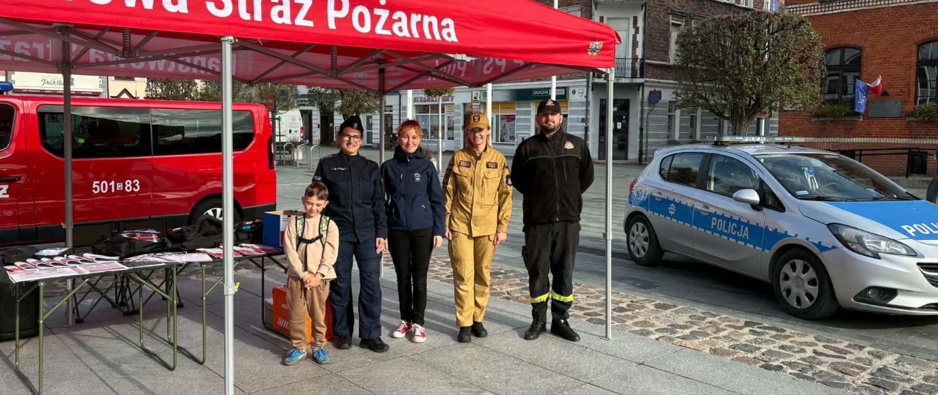 Na zdjęciu osoby odpowiedzialne za przygotowanie stoiska na piknik rodzinny funkcjonariusze KP PSP w Pucku, Funkcjonariuszka KPP w Pucku, oraz pracownik Urzędu Miasta w Pucku. 