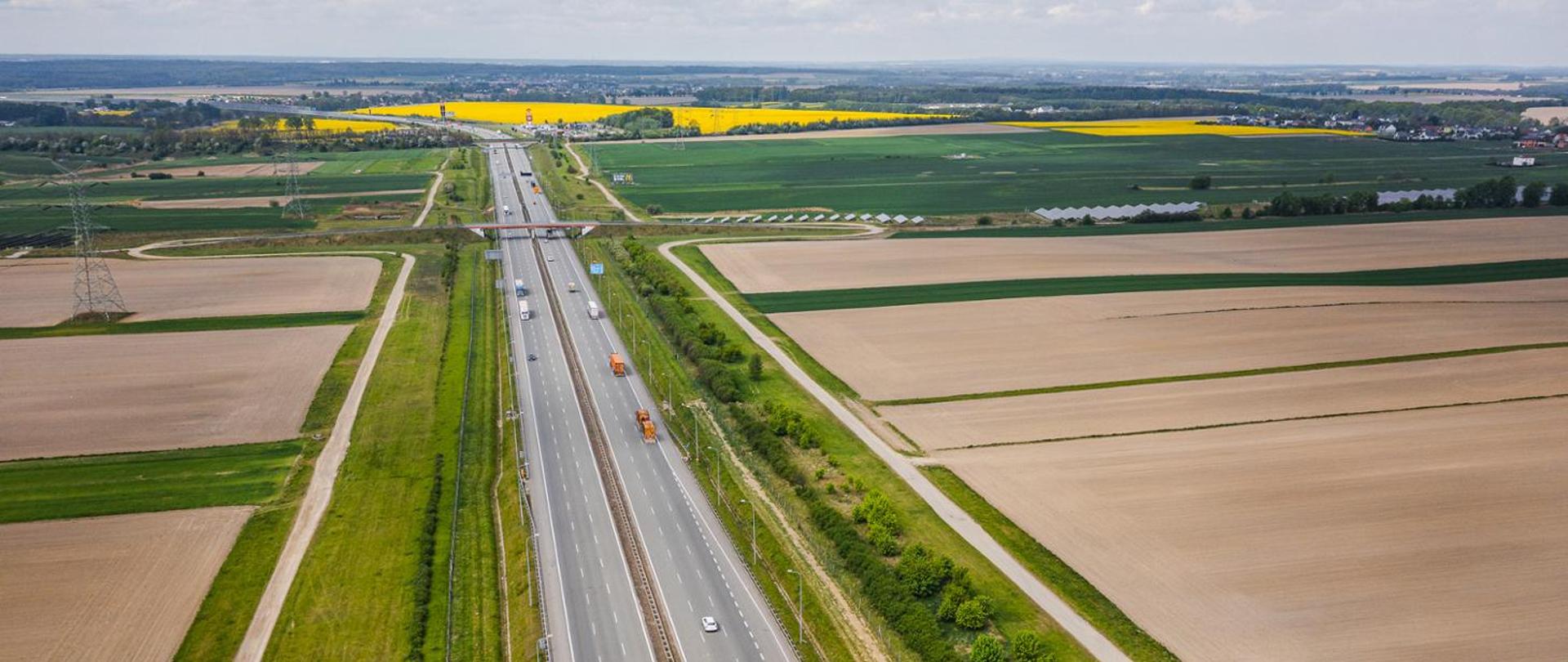 Trzypasowa autostrada A1 o nawierzchni bitumicznej z lotu ptaka. W tle wiadukt nad trasą główną oraz miejsca obsługi podróżnych.
