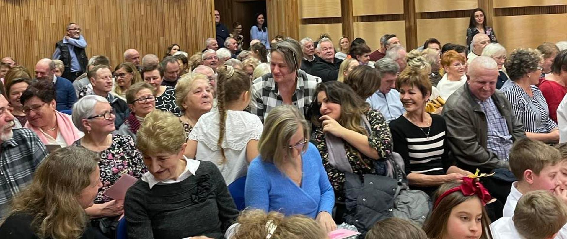 Zdjęcie ludzi siedzących na sali koncertowej. W tle panele akustyczne sali.