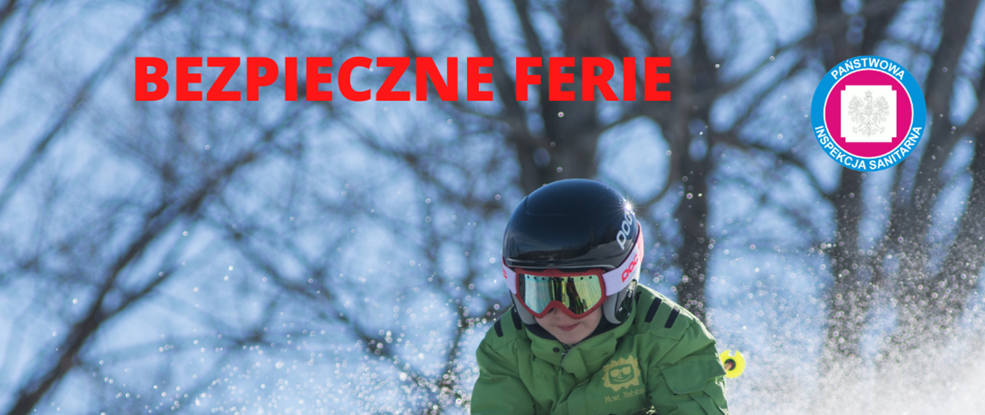 Na zdjęciu znajduje się chłopiec, który zjeżdża na nartach z obsypanego śniegiem stoku. Jest ciepło obrany, ma google, kask i rękawiczki. Uśmiecha się. 