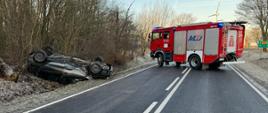 samochód osobowy leży na dachu, na poboczu drogi, samochód GBA 3/16 stoi w poprzek drogi blokując przejazd na czas prowadzenia działań.