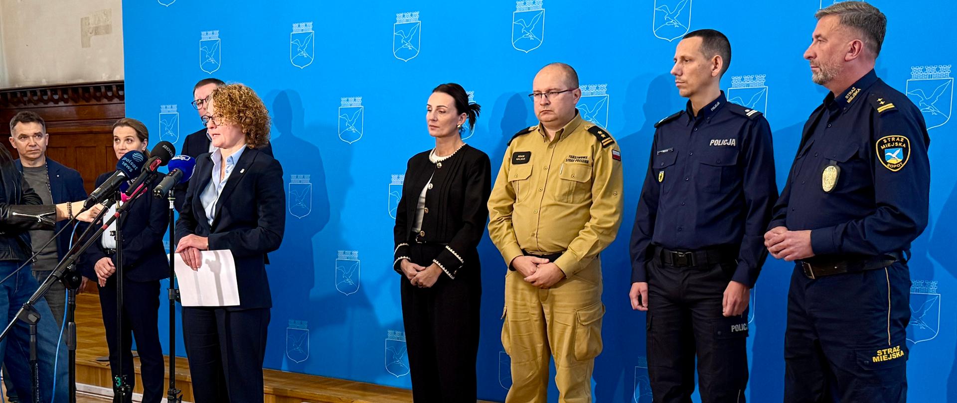 kila osób w tym policjanci i strażacy odpowiadają na pytania dziennikarzy podczas konferencjo poświęconej bezpieczeństwie