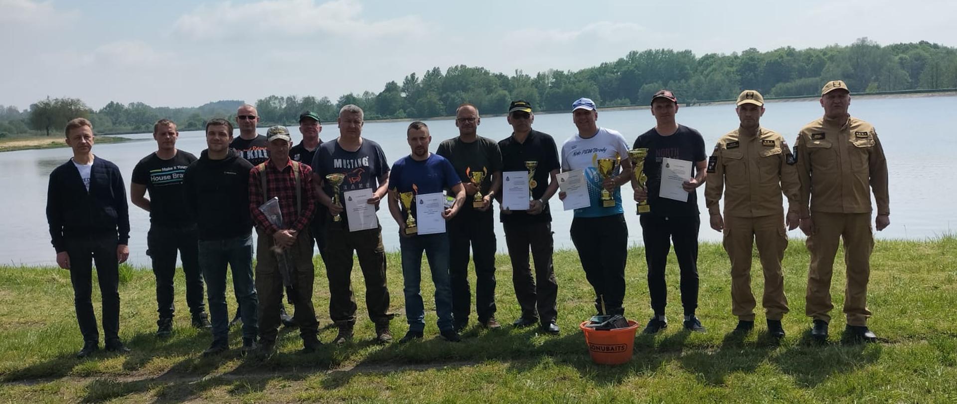 Zdjęcie przedstawia zawodników na tle zbiornika wodnego.