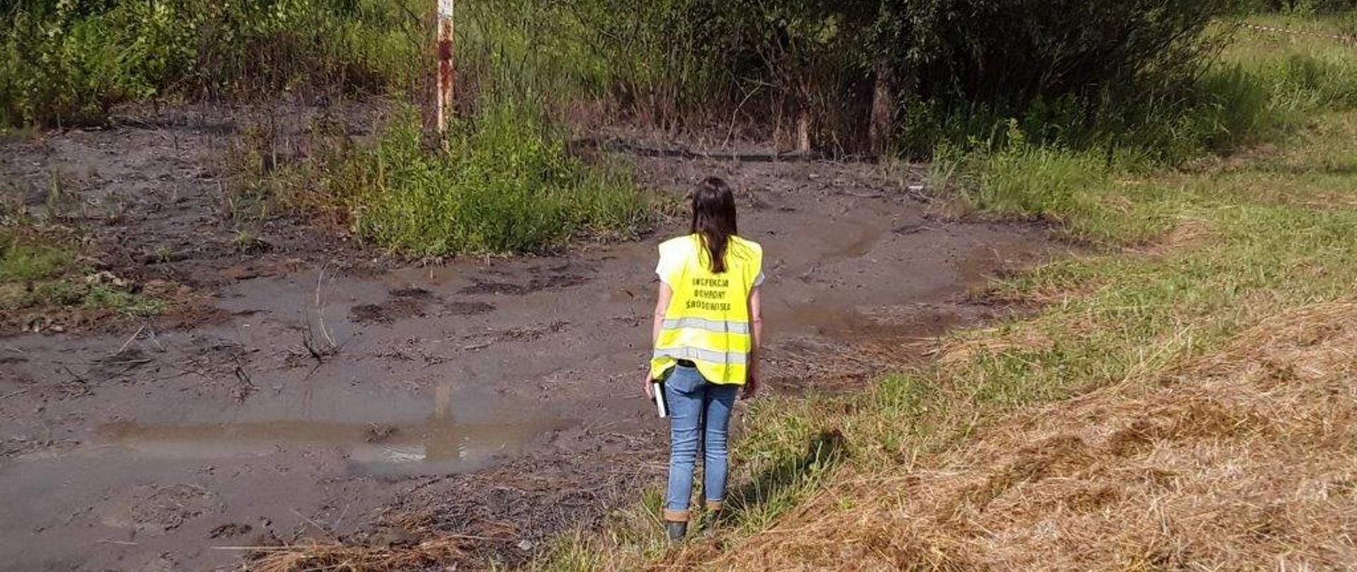 Inspektor Ochrony Środowiska stoi na brzegu zanieczyszczonego zbiornika.