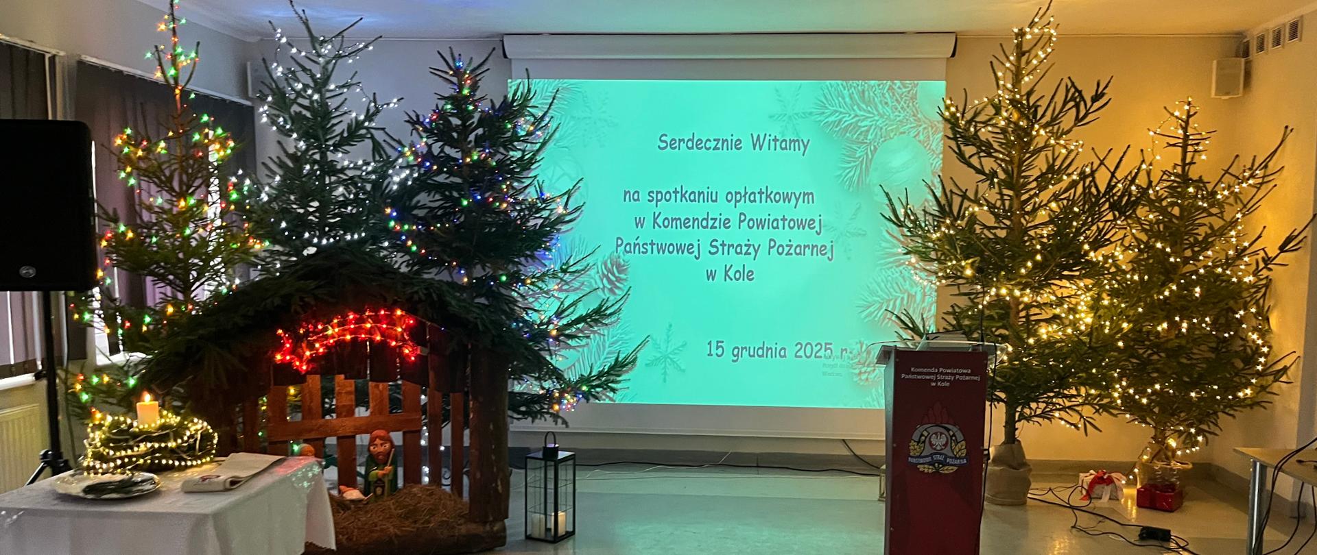 Zdjęcie przedstawia świetlicę komendy powiatowej PSP w Kole, choinki, stół z opłatkiem, stajenkę
