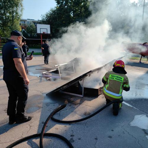 Na placu szkoleniowym gaszony jest panel fotowoltaiczny, widać strażaka oraz ludzi w mundurach z flagą Ukrainy