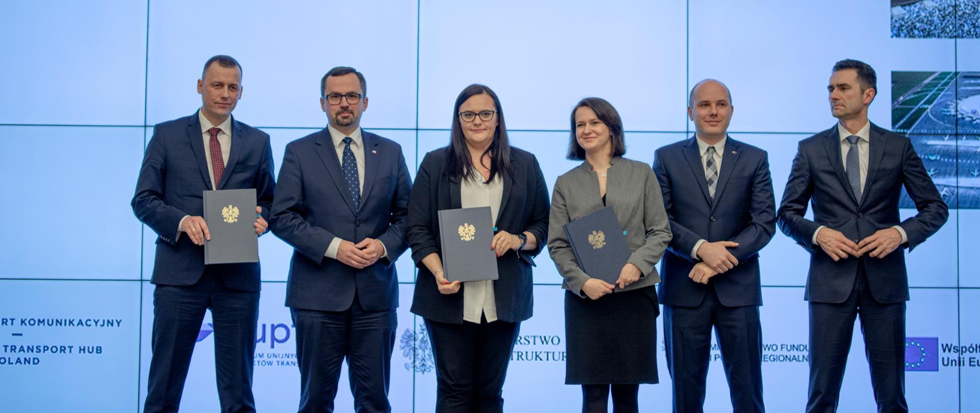 Zdjęcie grupowe z podpisanymi umowami, wśród osób m.in. minister Jarosińska-Jedynak, dyrektor Lech, prezes Wild, minister Horała