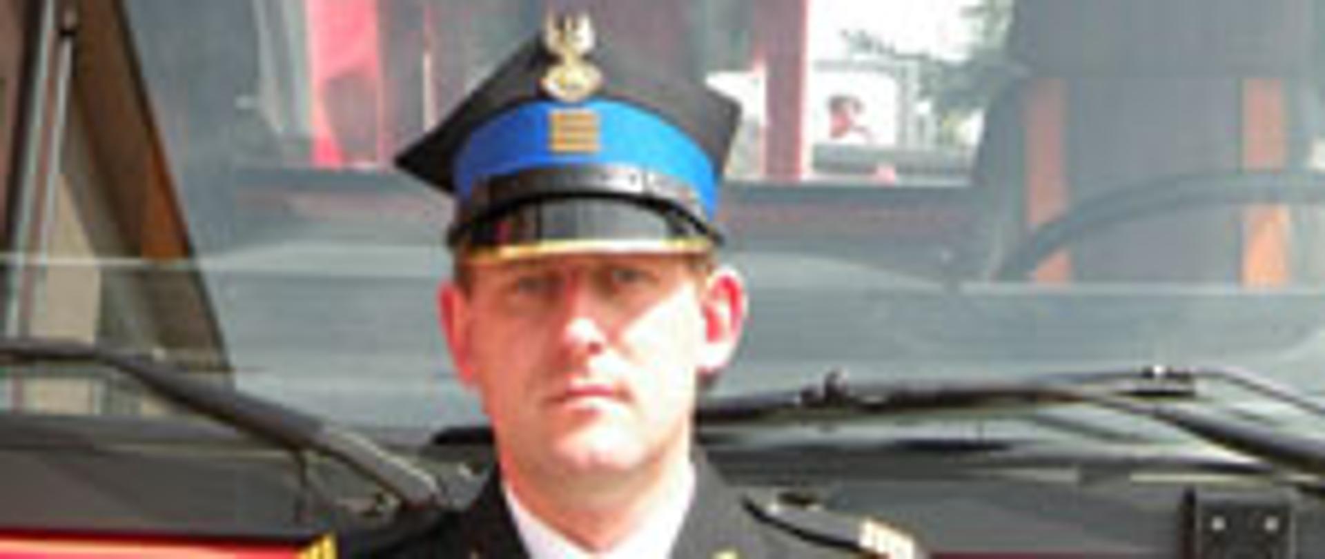 Na zdjęciu stoi strażak pozujący do zdjęcia