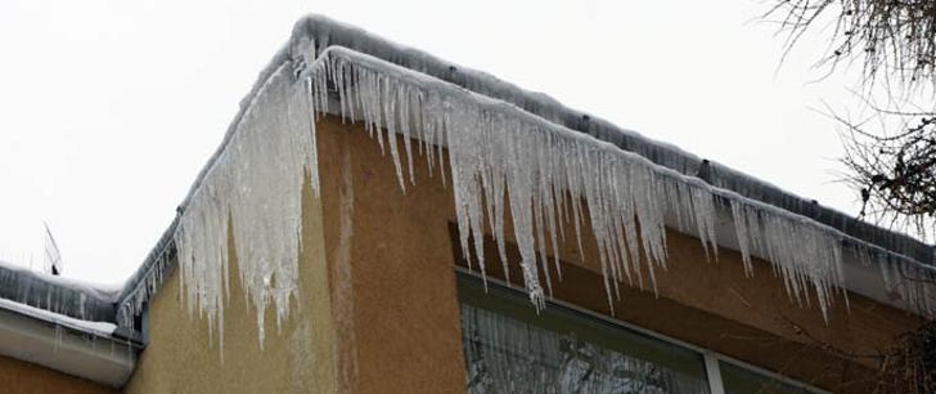 Obrazek przedstawia nawisy lodowe na dachu budynku.