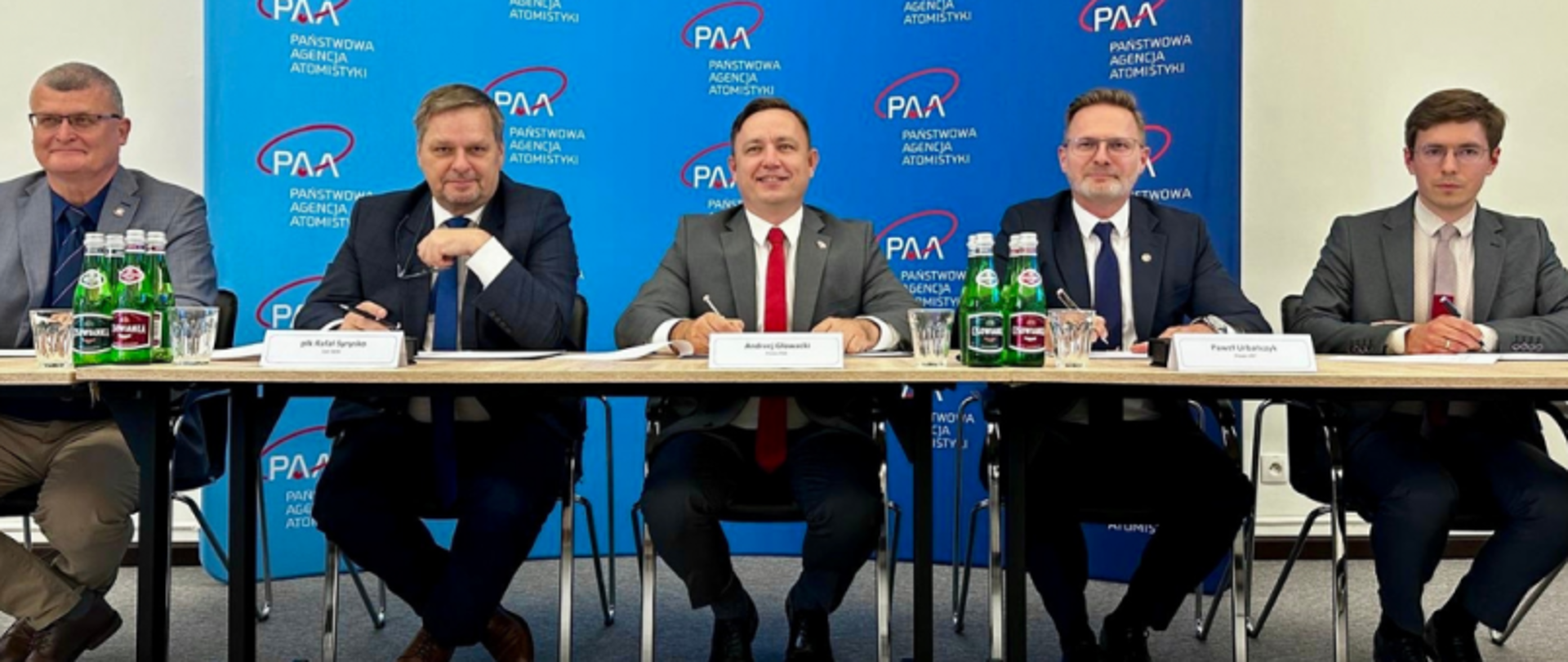 Przedstawiciele GUNB i PAA podczas spotkania w sprawie koordynacji kontroli nad obiektami jądrowymi. Uczestnicy siedzą przy stole na tle ścianki z logotypem Państwowej Agencji Atomistyki.
