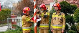 Poczet flagowy składający się z trzech strażaków JRG Wadowice w ubraniach specjalnych koloru piaskowego wciąga na maszt flagę państwową.