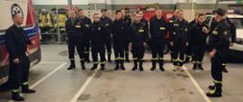 W centralnej części - uczestnicy szkolenia stoją w garażu JRG, po lewej i prawej stronie strażak PSP.