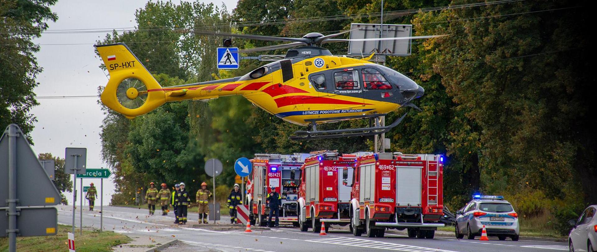 na miejscu widoczny jest startujący śmigłowiec LPR, z tyłu zaparkowane samochody pożarnicze