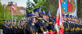Kompania honorowa Akademii Pożarniczej stoi w szyku podczas uroczystego apelu. Na pierwszym planie poczet sztandarowy, a strażacy w mundurach galowych oddają honory.
