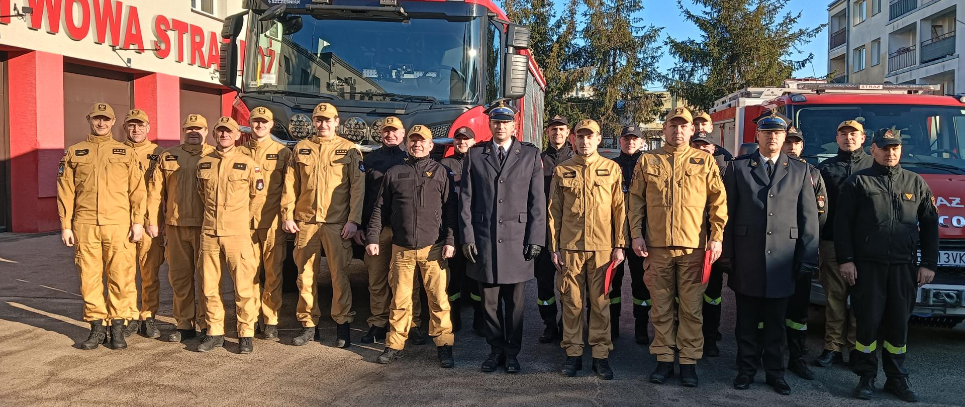 Wspólne zdjęcie funkcjonariuszy na tle wozów strażackich