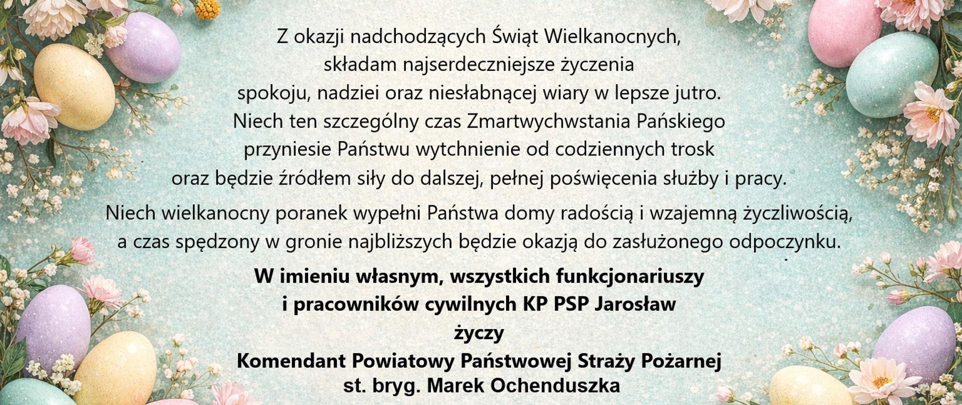 Grafika z życzeniami wielkanocnymi na jasnym tle ozdobionym pastelowymi pisankami i wiosennymi kwiatami rozmieszczonymi wokół krawędzi. W centrum znajduje się tekst życzeń z okazji Świąt Wielkanocnych, zawierający słowa o spokoju, nadziei, wierze, odpoczynku i radości w gronie bliskich. Życzenia składane są w imieniu funkcjonariuszy i pracowników cywilnych Komendy Powiatowej PSP w Jarosławiu przez Komendanta Powiatowego Państwowej Straży Pożarnej, st. bryg. Marka Ochenduszka. Na dole widoczne jest godło Państwowej Straży Pożarnej.