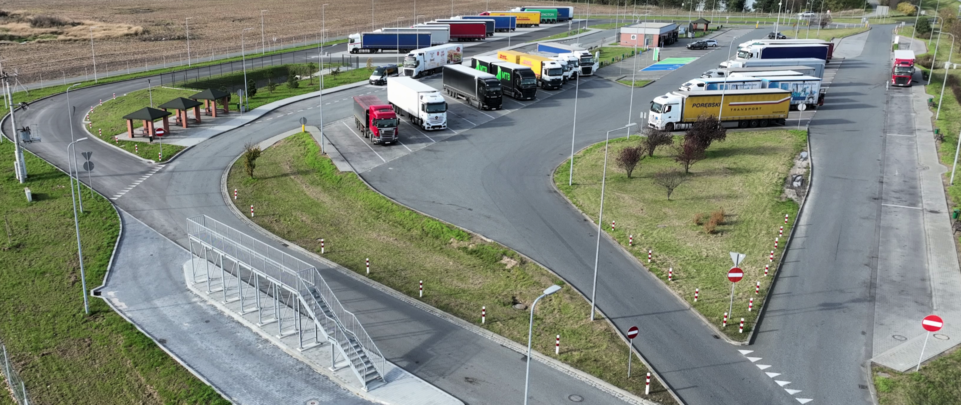 Parking dla ciężarówek na MOP Prószków. Na miejscach parkingowych parkujące samochody. Na pierwszym planie rampa do odśnieżania samochodów ciężarowych. 