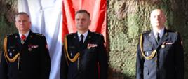 Zdanie i przyjęcie obowiązków Komendanta Miejskiego Państwowej Straży Pożarnej w Białymstoku - na zdjęciu dotychczasowy komendant miejski PSP w Białymstoku, podlaski komendant wojewódzki PSP i nowy komendant miejski PSP w Białymstoku, stoją przy ścianie, w tle barwy narodowe