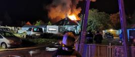 Zdjęcie wykonane porą nocną. Przedstawia działania jednostek ochrony przeciwpożarowej w związku z pożarem poddasza budynku wolnostojącego w trakcie budowy.