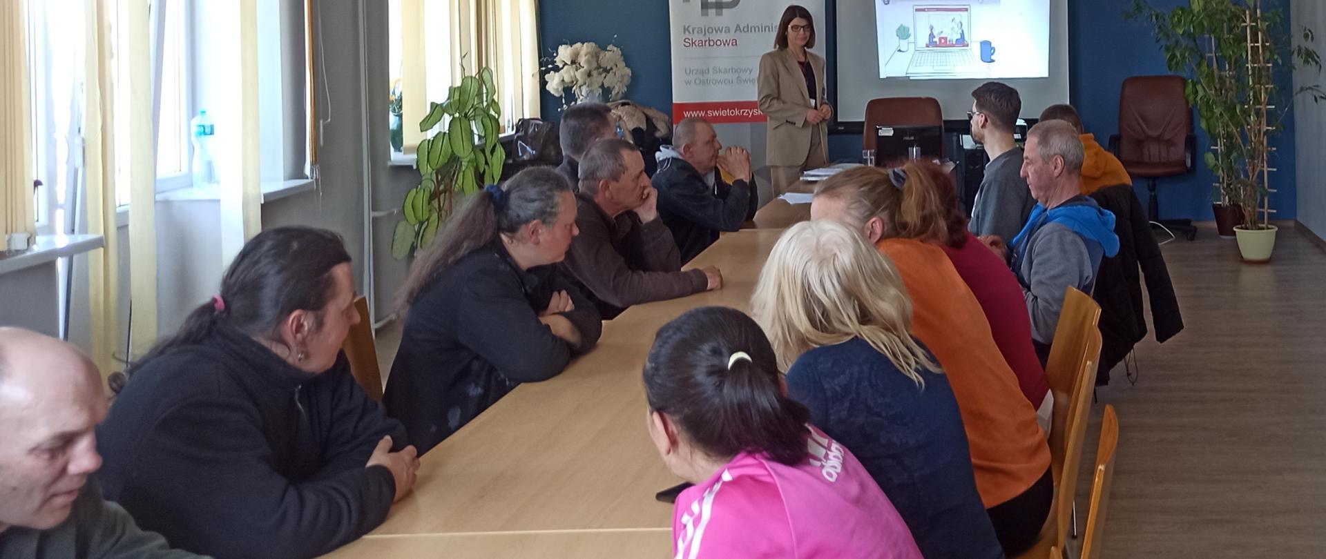 Przy stole siedzi grupa osób i słucha wykładu o podatkach