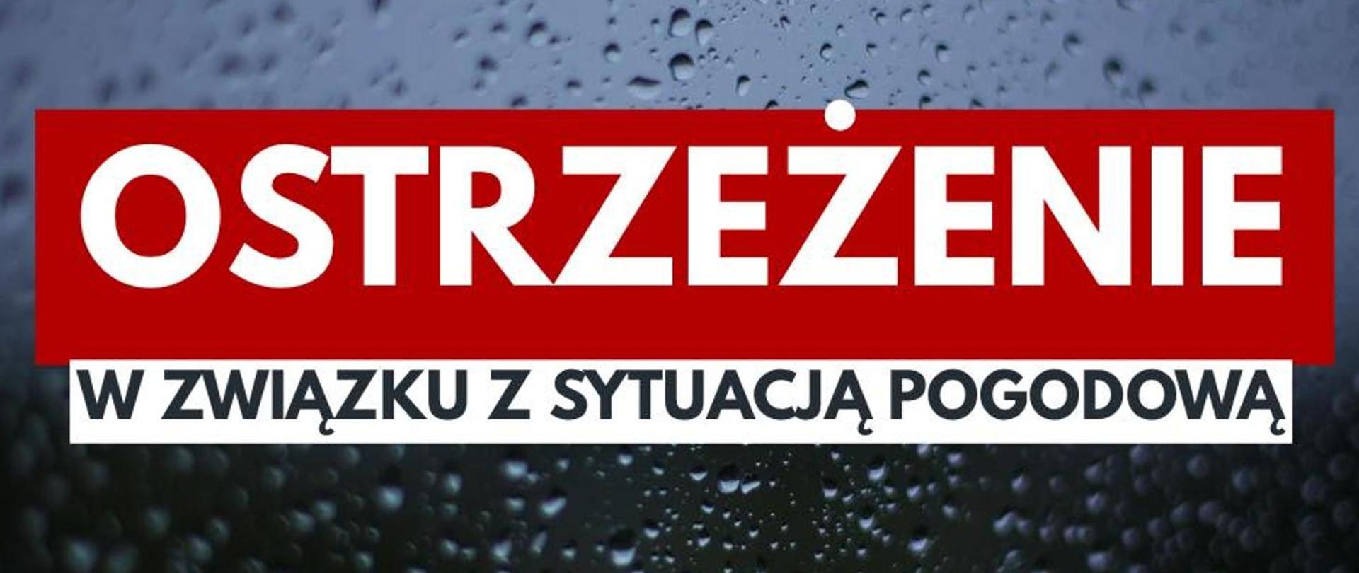 W tle szyba na której widoczne są krople wody. Na pierwszym planie napis :"Ostrzeżenie w związku z sytuacją pogodową" "Ostrzeżenie" napisane na czerwonym pasie - wielkimi białymi literami. poniżej pozostała część napisy napisana czarną czcionką na białym pasku. 
