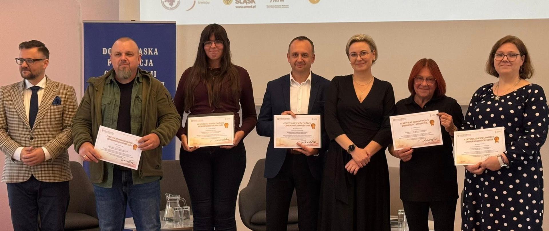 Konferencja regionalna programu Moc Małych Społeczności w Krzyżowej. Na zdjęciu Sekretarz Stanu Adriana Porowska z uczestnikami spotkania. Uczestnicy prezentują certyfikaty Twórców Odporności Społecznej.