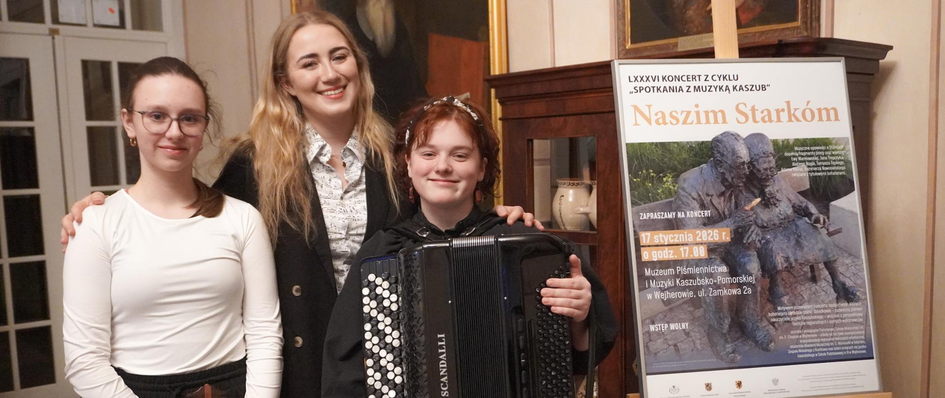 Pani Zofia Marszk wraz z dwoma uczennicami pozuje do zdjęcia przed koncertem w muzeum. Dziewczynki trzymają swoje instrumenty: gitarę oraz akordeon.