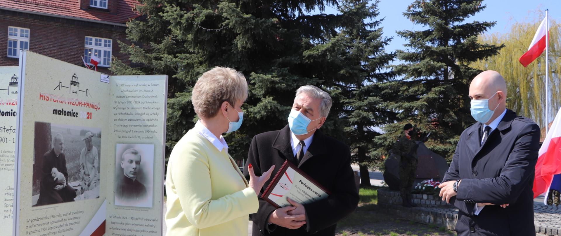 Wicewojewoda rozmawia z burmistrz Małomic, w tle powiewają biało-czerwone flagi, widać również panel wystawy 