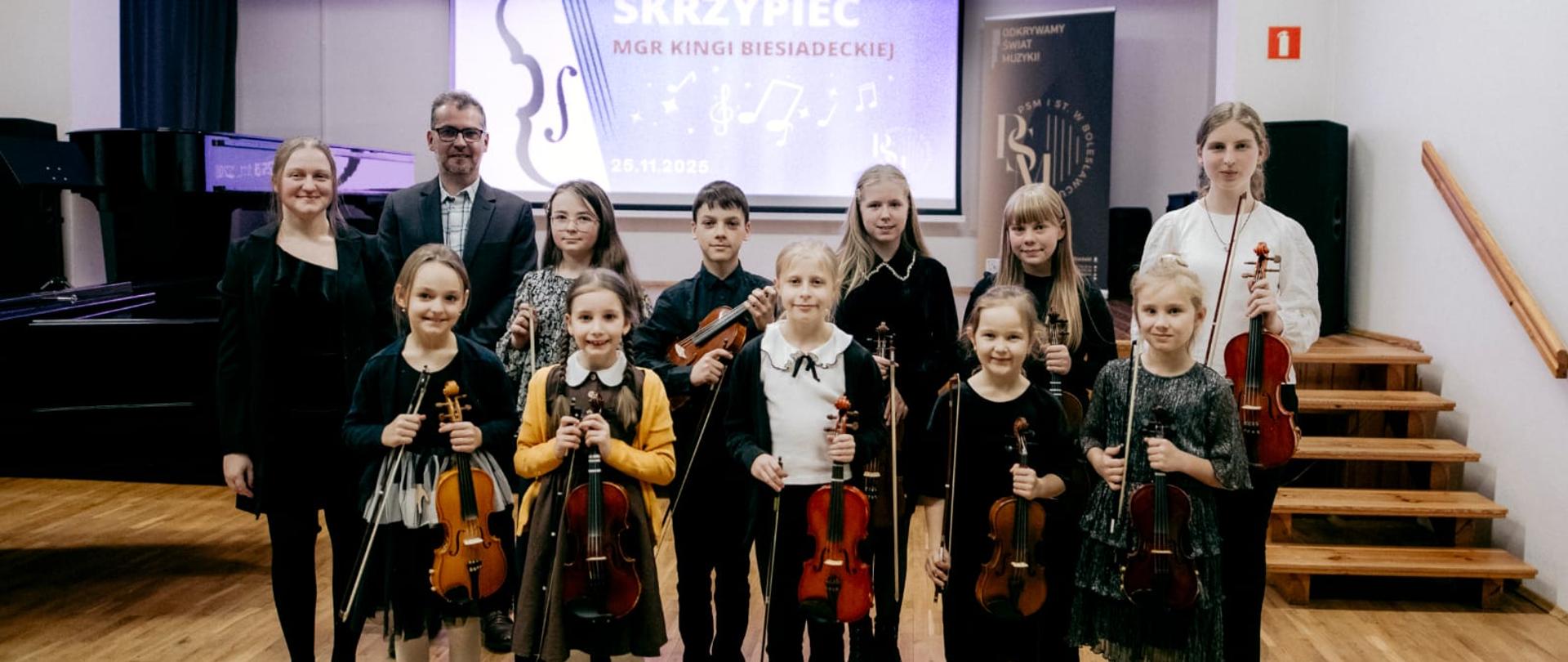 Zdjęcie przedstawiające wykonawców popisu klasy skrzypiec mgr Kingi Biesiadeckiej, który odbył się 25 listopada 2025 r. w auli szkoły.
