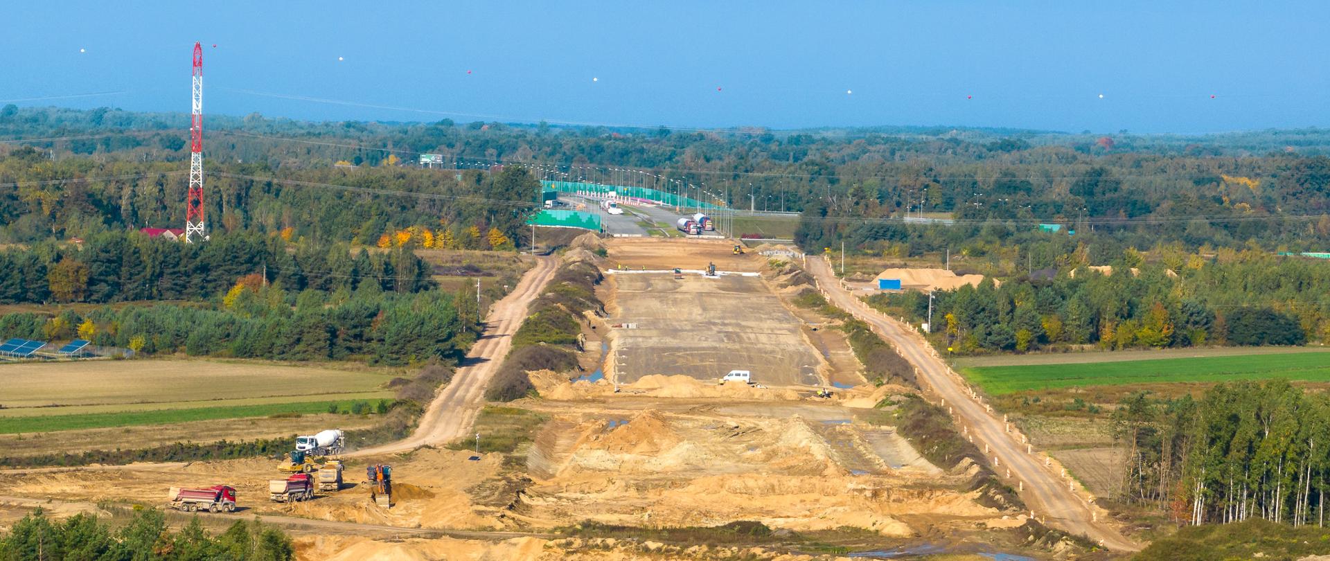 Widok na plac budowy autostrady A2. Wczesny etap prac. Widoczny szeroki pas oczyszczonej ziemi i przygotowanej podbudowy pod nową autostradę. W tle, na horyzoncie widoczne już gotowe pasy ruchu.