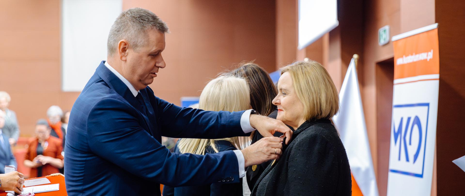 Wpinanie odznaczenia w klapę marynarki. Kolejni nagrodzeni otrzymują medale 