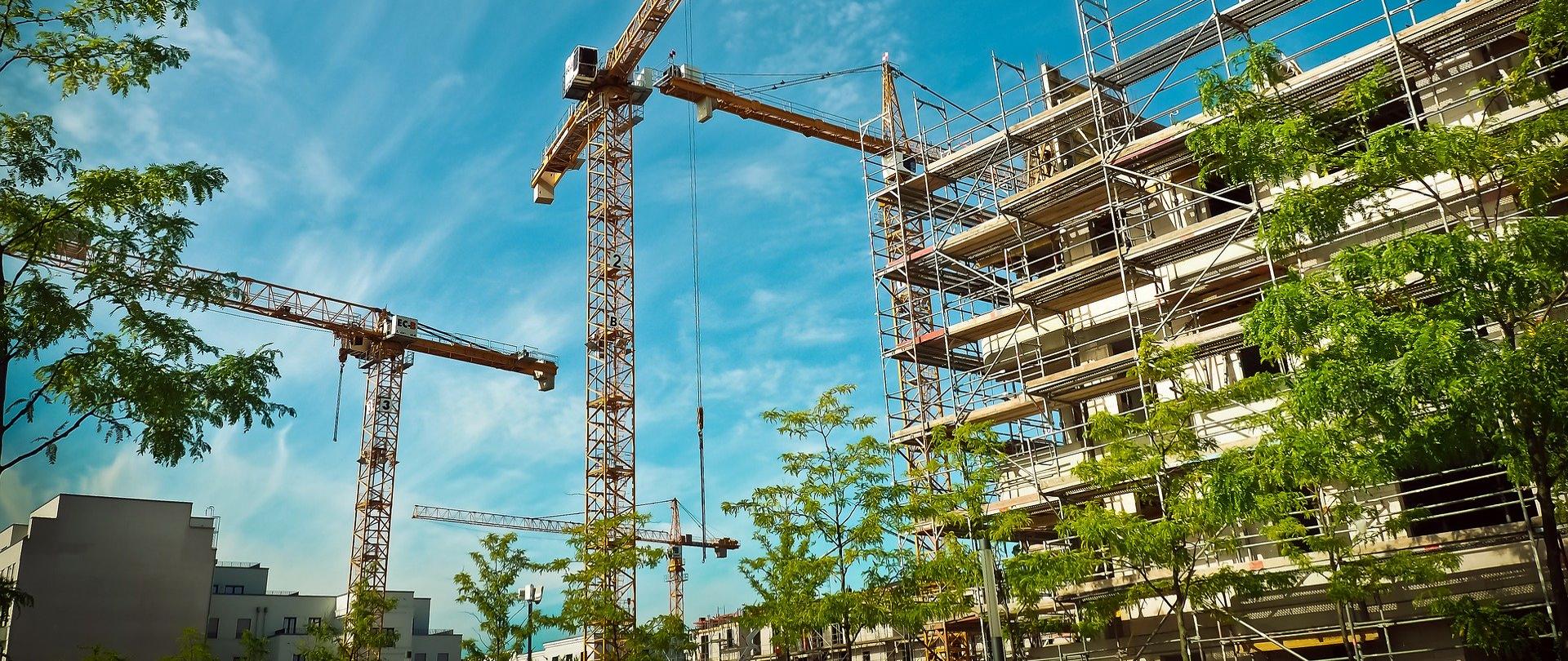 Na zdjęciu bloki mieszkalne w budowie, rusztowania i dźwigi