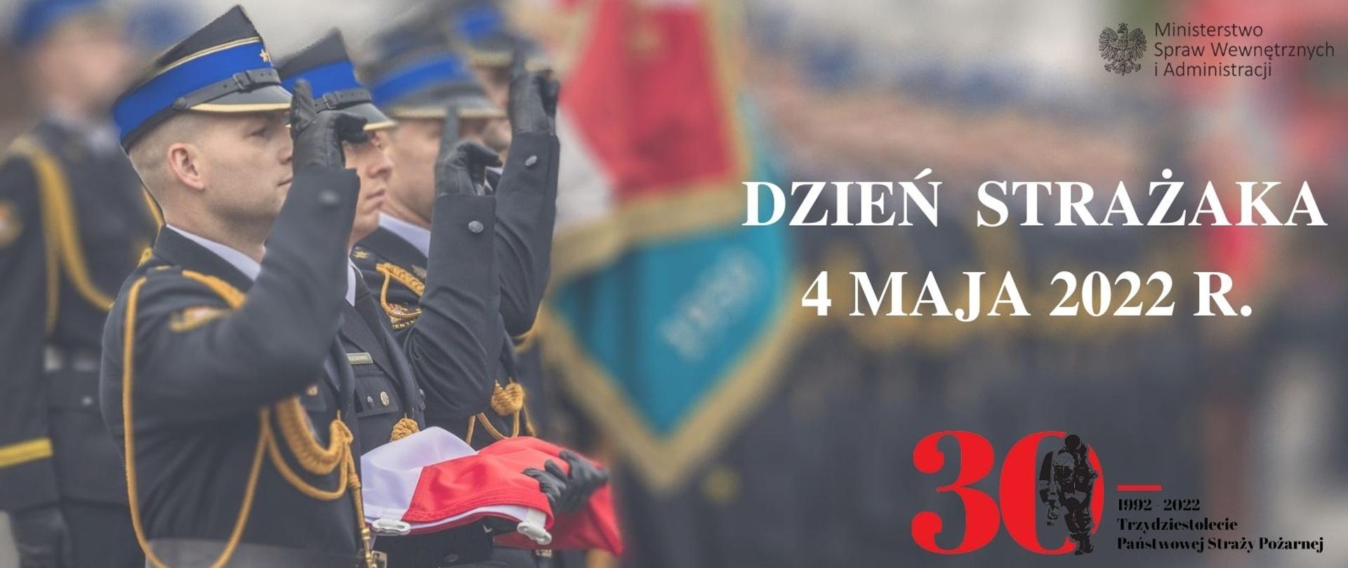 Infografika z okazji dnia strażaka - po lewo kilku strażaków salutuje, drugi pod lewej trzyma na dłoniach złożoną flagę RP, po prawej stronie napis DZIEŃ STRAŻAKA 4 MAJA 2022 R. , pod spodem logotyp 30lecia PSP, w prawym górnym rogu logo MSWiA