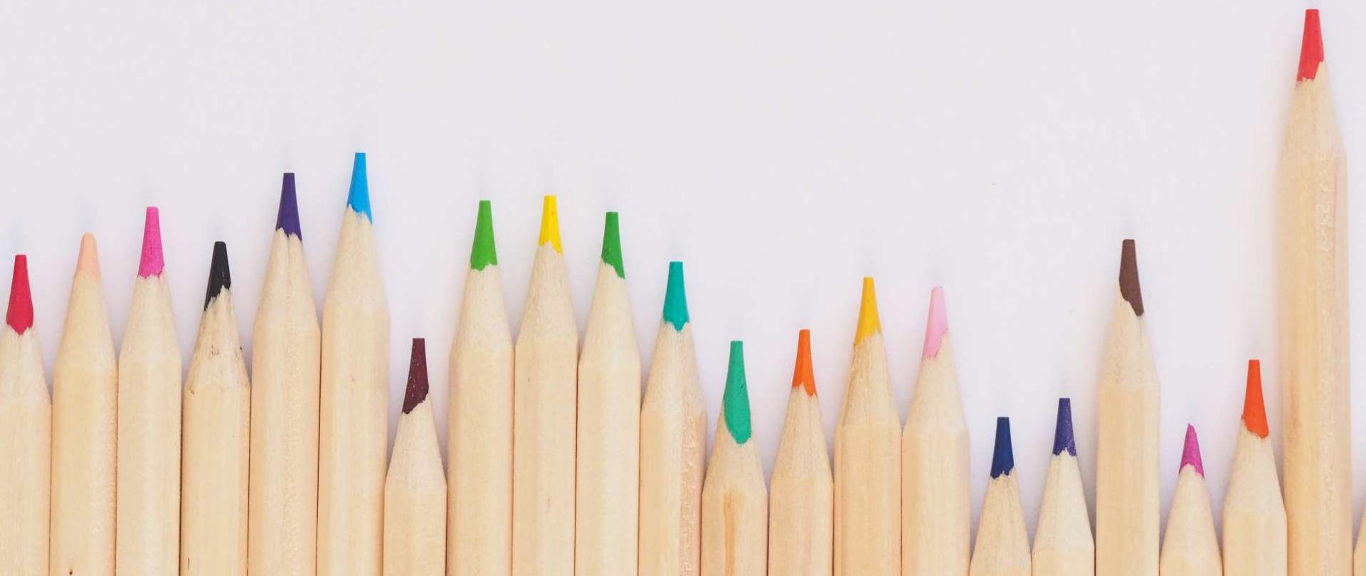 w dolnej części drewniane kredki z różnokolorowymi rysikami na jasnoszarym tle