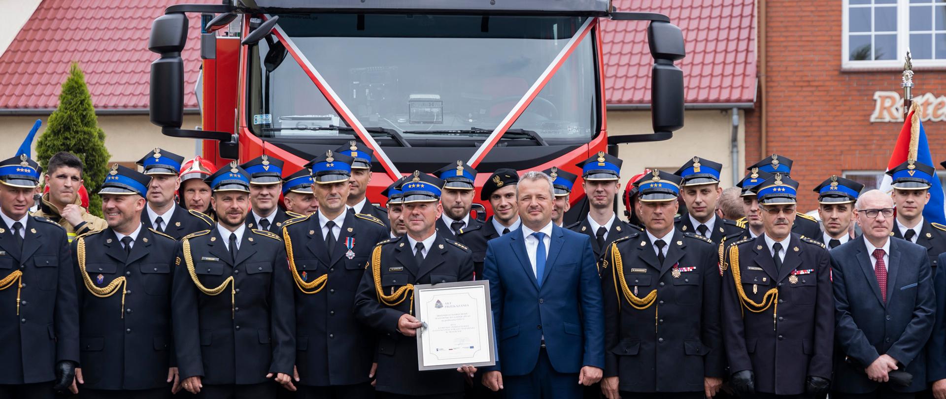 
Tłum ludzi stojący na placu przed strażą pożarną
