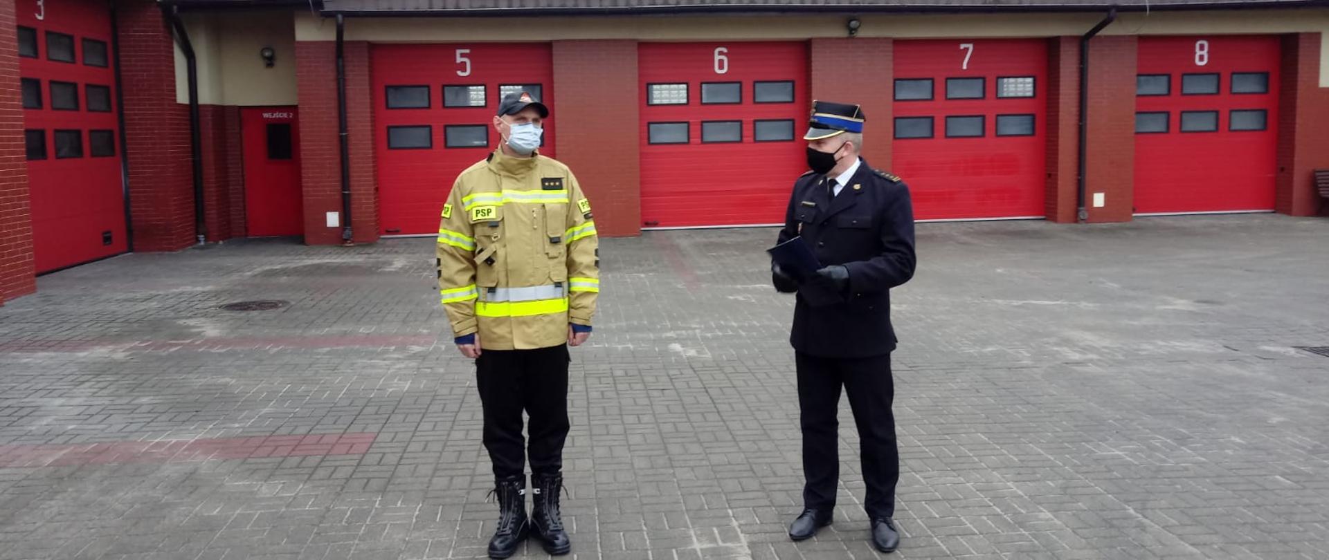 Na placu Jednostki Ratowniczo-Gaśniczej Państwowej Straży Pożarnej w Rypinie, podczas zmiany służby, asp. sztab. Rafał Pankowski odbiera gratulacje z rąk Komendanta Powiatowego st. bryg. Grzegorza Łydkowskiego. W tle garaże JRG.
