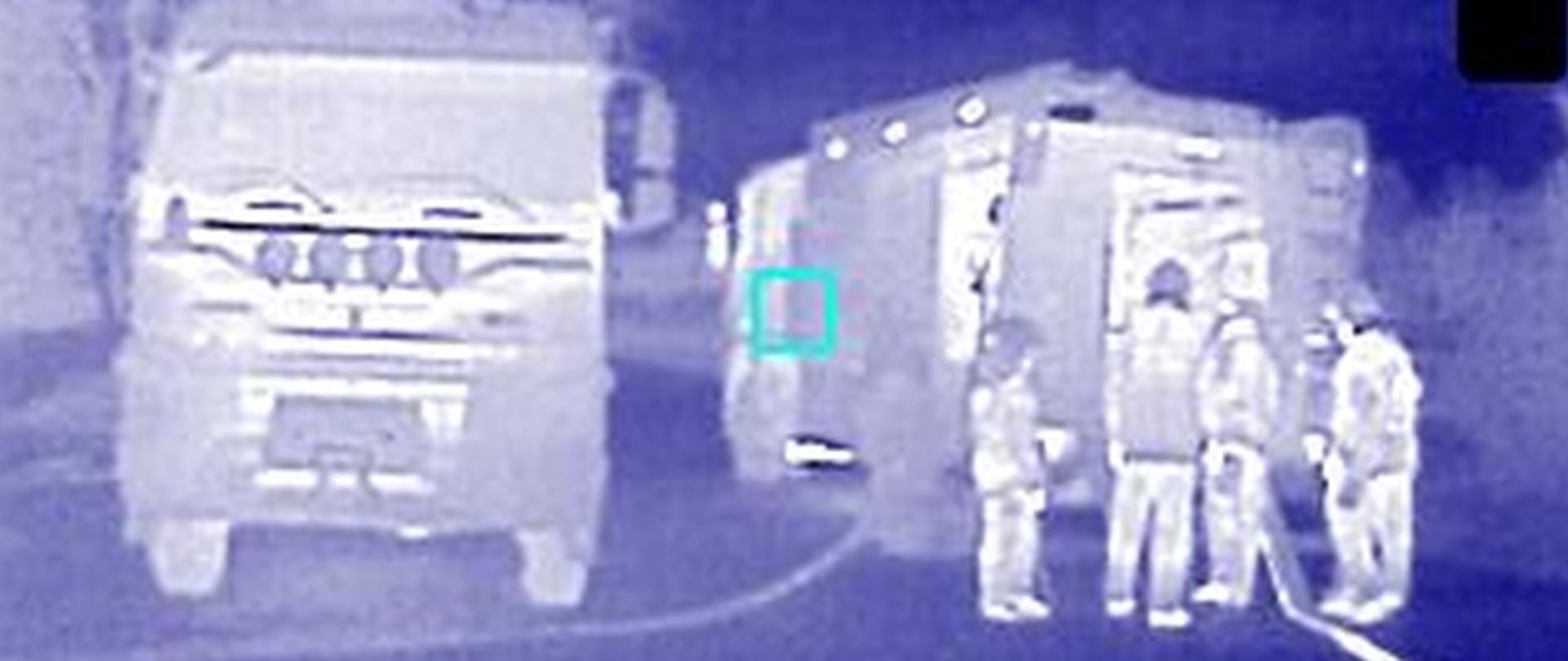 Zdjęcie z kamery termowizyjnej na którym widać dwa samochody bojowe, przy jednym z pojazdów stoją strażacy