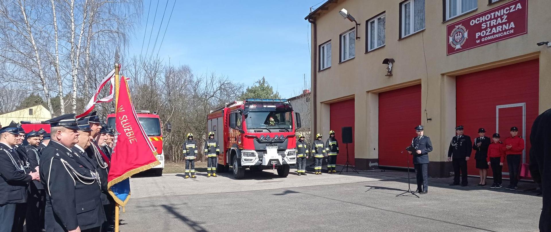 Pododdziały w trakcie uroczystości przed strażnicą OSP Gomunice. Na pierwszym planie poczty sztandarowe.