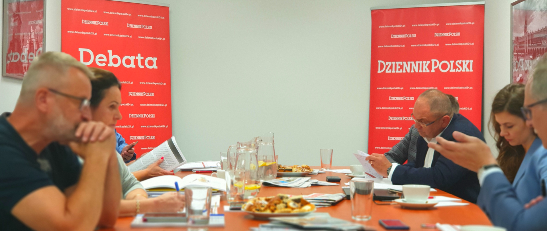 Uczestnicy debaty siedzą po dwóch stronach stołu