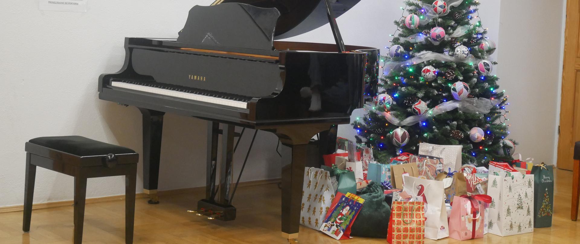Bursowa świetlica. Przy fortepianie stoi choinka o obok niej góra prezentów.