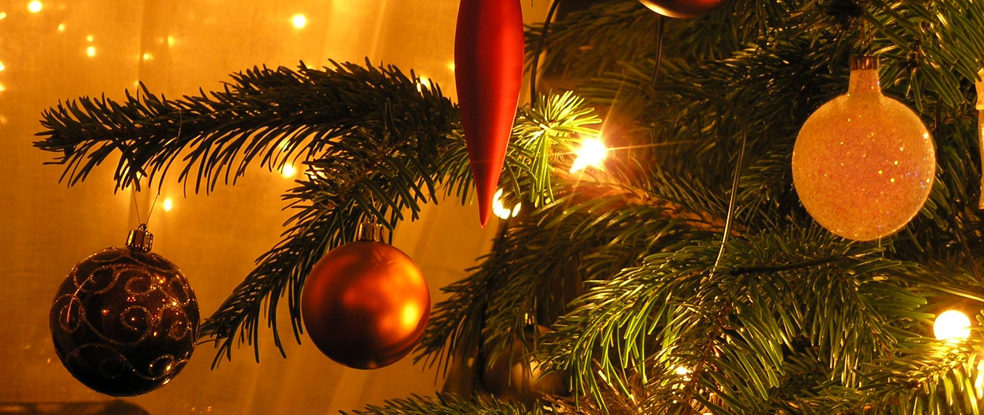 Fragment choinki ze zbliżeniniem na wiszące na niej bombki i lampki.