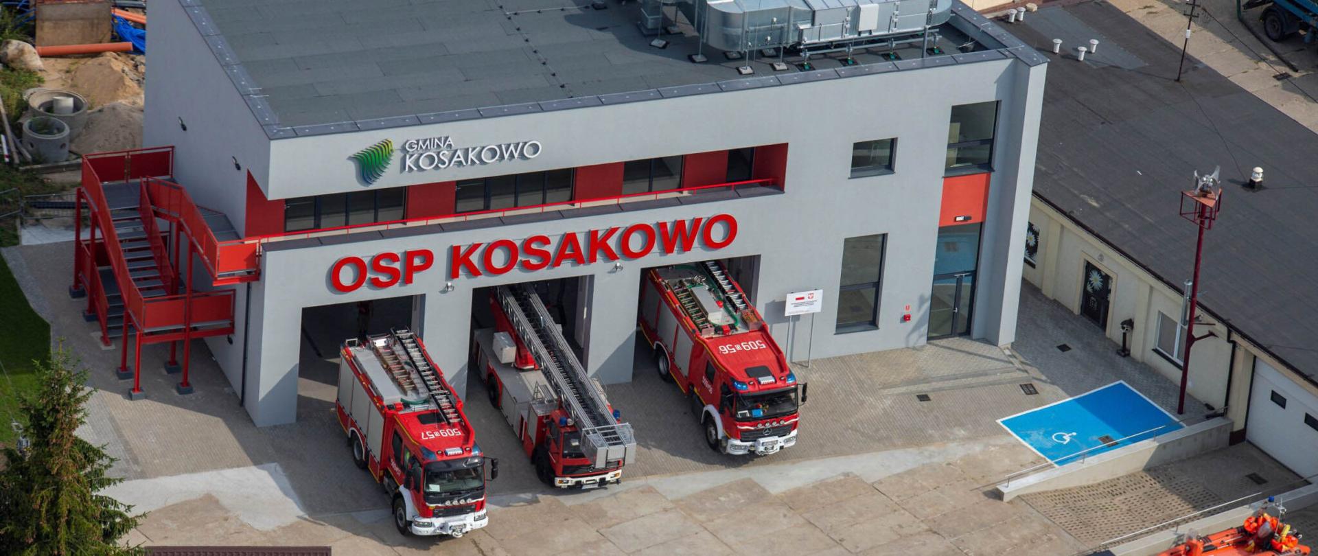 Zdjęcie zrobione z góry, na którym widać nowa strażnicę Ochotniczej Straży Pożarnej Kosakowo. Przed wjazdami stoją trzy samochody strażackie,