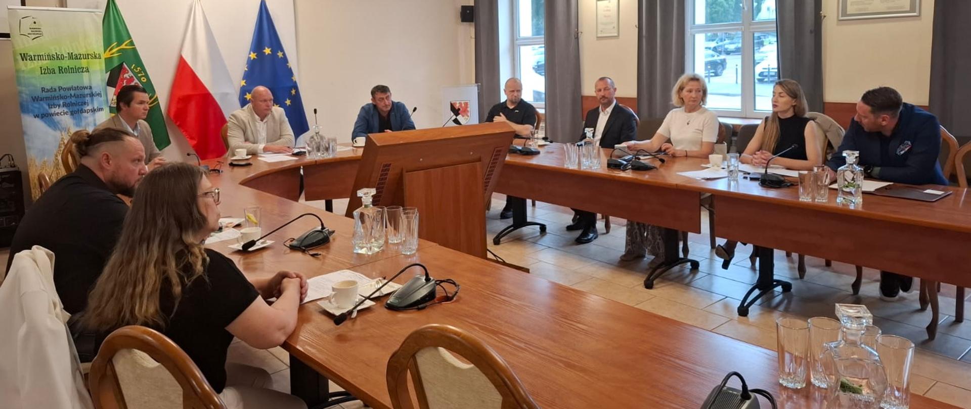 Grupa osób siedzi przy stole, w głębi ekran, flagi, baner WMIR