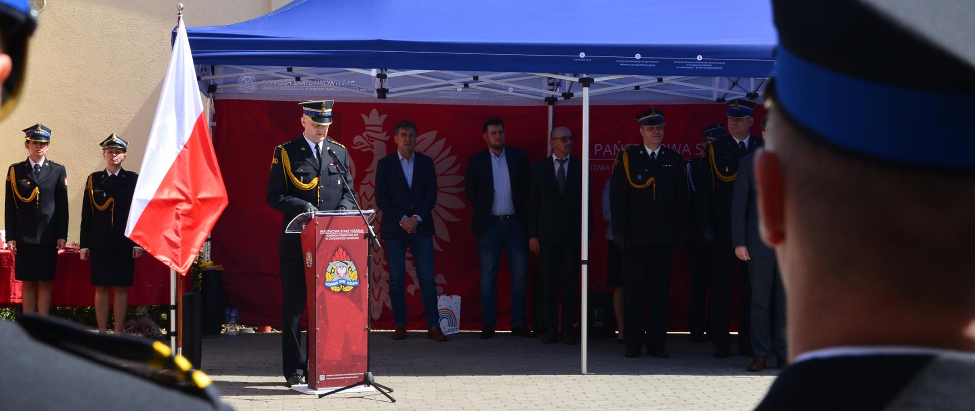 Zdjęcie przedstawia Komendanta Powiatowego podczas powitania, w tle namiot i zaproszeni goście