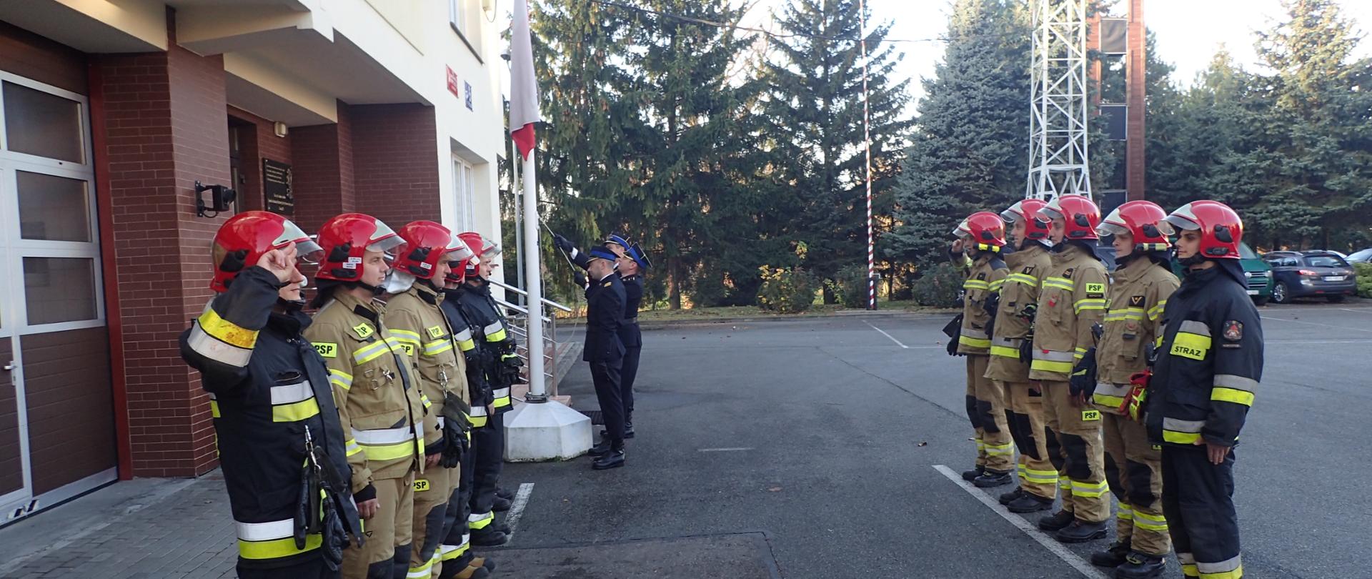 Podniesienie Flagi na maszt z okazji 103 rocznicy odzyskania niepodległości. Poczet flagowy w umundurowaniu galowym. W tle zbiórka strażaków w umundurowaniu bojowym. 