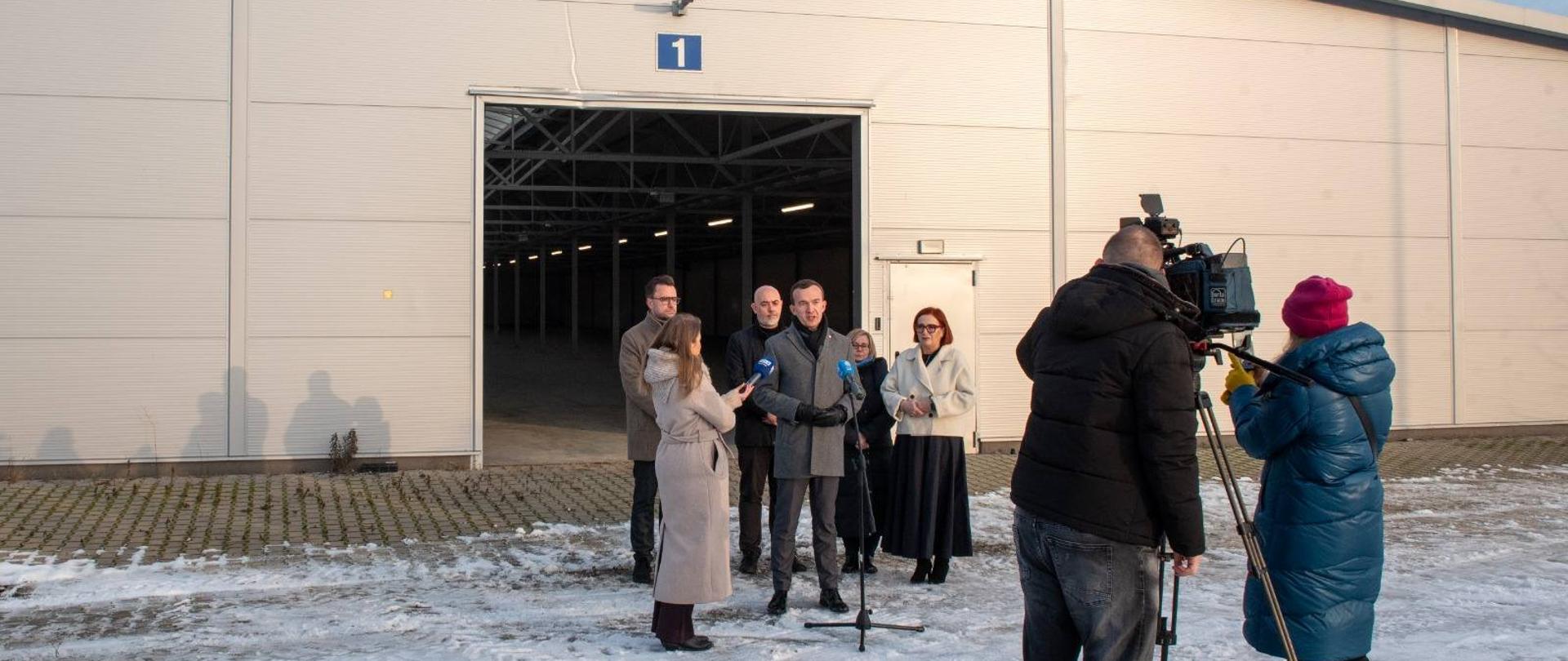 Kilka osób stoi przed halą magazynową 