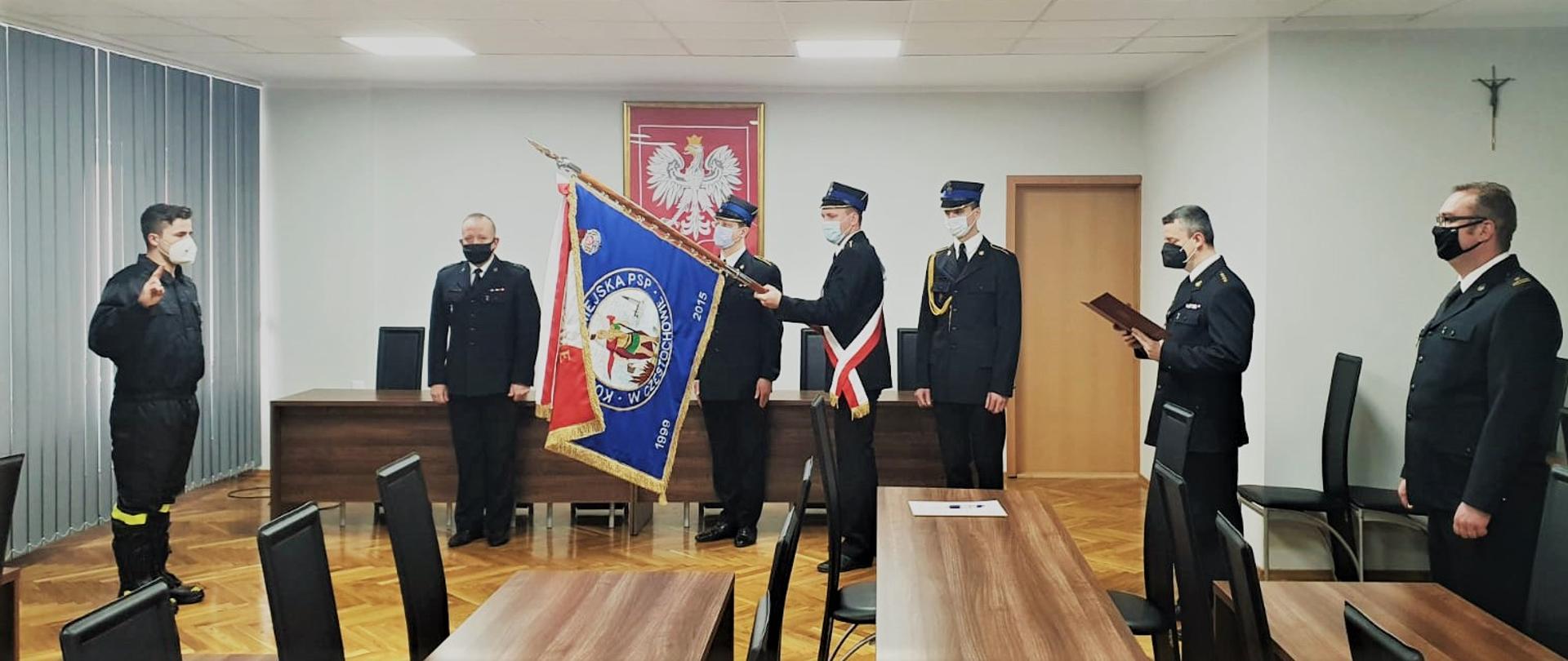 Zdjęcie przedstawia funkcjonariuszy Państwowej Straży Pożarnej podczas uroczystego ślubowania. Na zdjęciu widoczni funkcjonariusze w mundurach wyjściowych oraz sztandar Komendy Miejskiej w Częstochowie. 