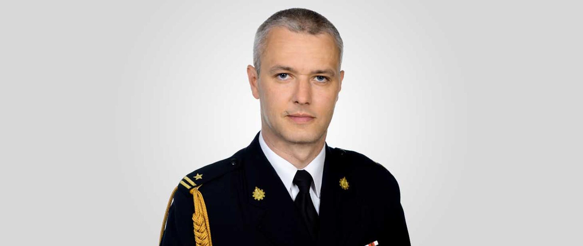 zdjęcie portretowe zastępcy komendanta mł. bryg. Sebastiana Łukowicza na jasnym tle w mundurze galowym