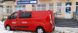 Przed przychodnią zdrowia stoi zaparkowany samochód osobowy pożarniczy. Aura zimowa. Przychodnia znajduje się na parterze w budynku mieszkalnym wielorodzinnym.